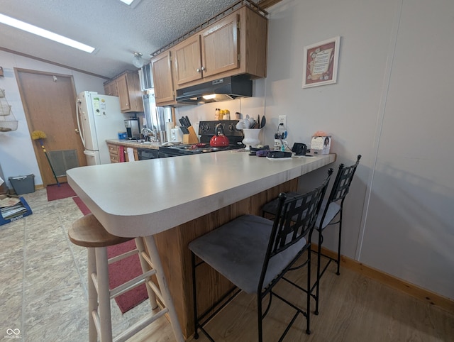 kitchen with black electric range oven, a textured ceiling, white refrigerator, a kitchen breakfast bar, and kitchen peninsula