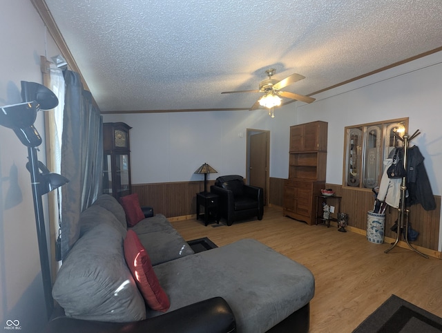 living room with ceiling fan, ornamental molding, light hardwood / wood-style floors, a textured ceiling, and wood walls