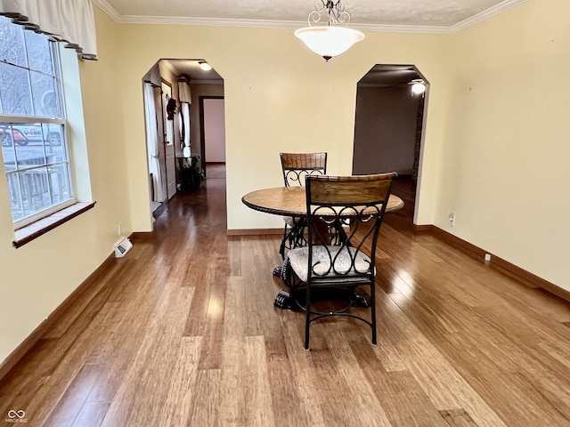 dining room with a wealth of natural light, arched walkways, wood finished floors, and crown molding