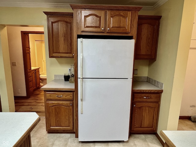 kitchen featuring brown cabinets, freestanding refrigerator, crown molding, light countertops, and baseboards