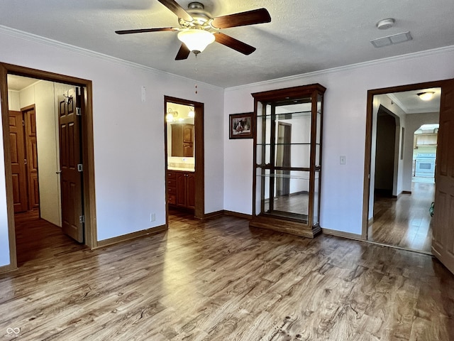 unfurnished room featuring visible vents, a textured ceiling, wood finished floors, crown molding, and baseboards