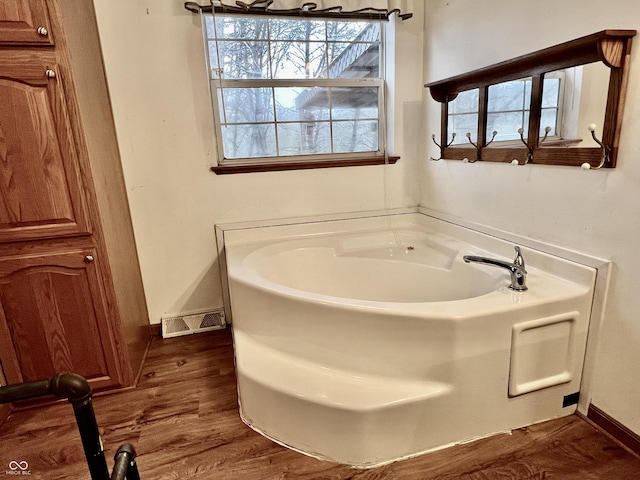 full bathroom with wood finished floors, plenty of natural light, a bath, and visible vents