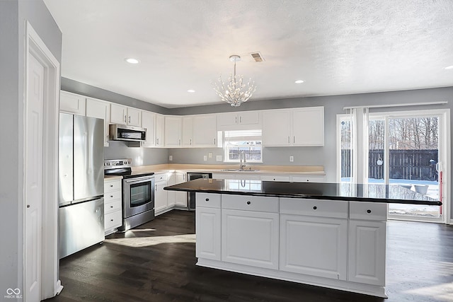 kitchen with decorative light fixtures, a center island, stainless steel appliances, and white cabinetry