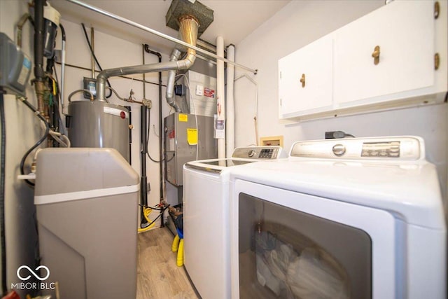 washroom with washer and clothes dryer, water heater, light hardwood / wood-style floors, and cabinets