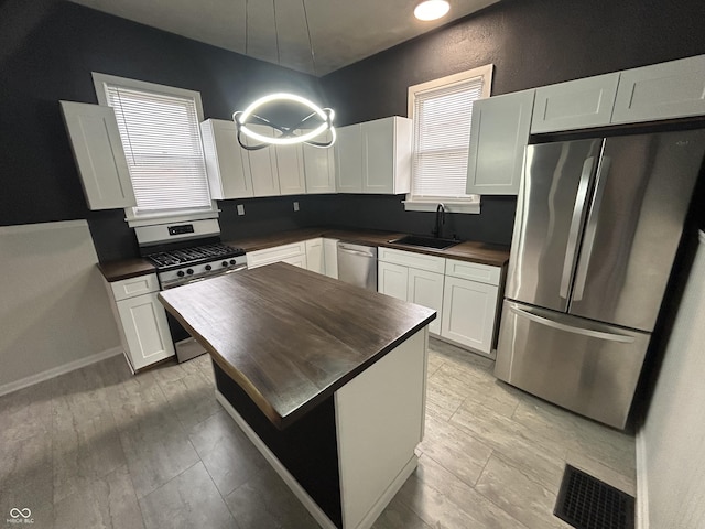 kitchen featuring sink, appliances with stainless steel finishes, a healthy amount of sunlight, white cabinets, and light wood-type flooring