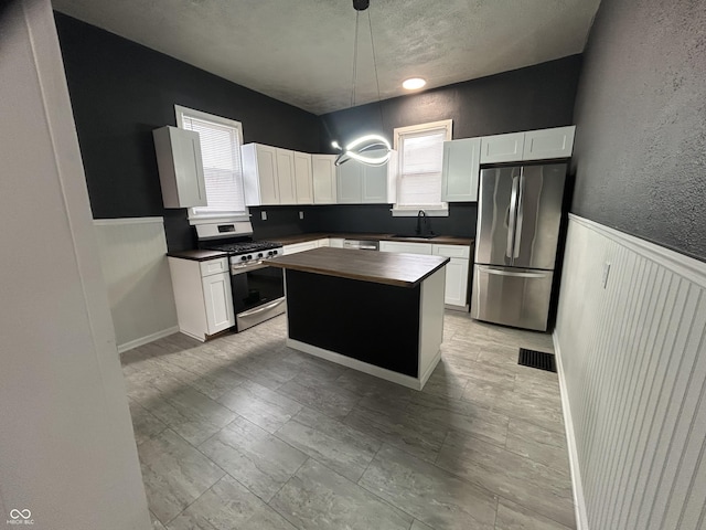 kitchen featuring pendant lighting, sink, white cabinetry, stainless steel appliances, and a kitchen island