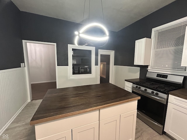 kitchen featuring stainless steel gas range oven, white cabinetry, black microwave, light hardwood / wood-style flooring, and pendant lighting