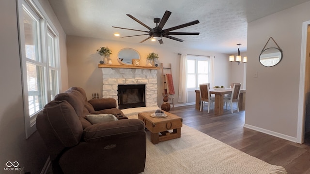 living room featuring hardwood / wood-style flooring, a stone fireplace, ceiling fan with notable chandelier, and a textured ceiling