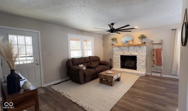 living room featuring dark wood-type flooring, a stone fireplace, a textured ceiling, and a wealth of natural light