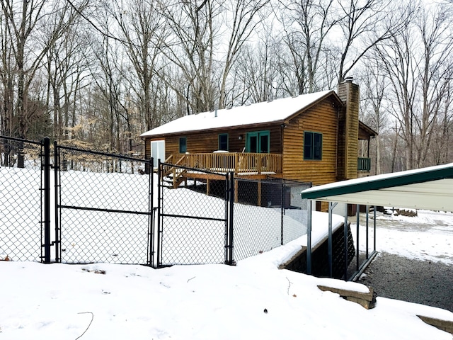 snow covered rear of property featuring a carport and a wooden deck