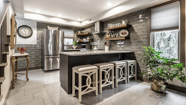 kitchen with open shelves, light stone counters, appliances with stainless steel finishes, a breakfast bar area, and a peninsula