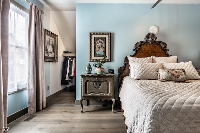 bedroom featuring light wood-type flooring, visible vents, a walk in closet, a closet, and baseboards