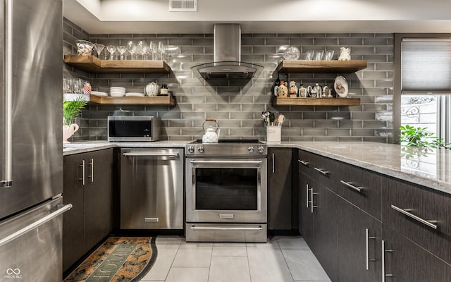 kitchen with tasteful backsplash, range hood, high end appliances, light stone countertops, and light tile patterned floors