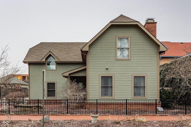 back of house featuring roof with shingles, a fenced front yard, and a chimney