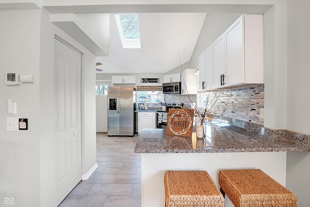 kitchen with white cabinets, vaulted ceiling with skylight, dark stone countertops, and stainless steel appliances