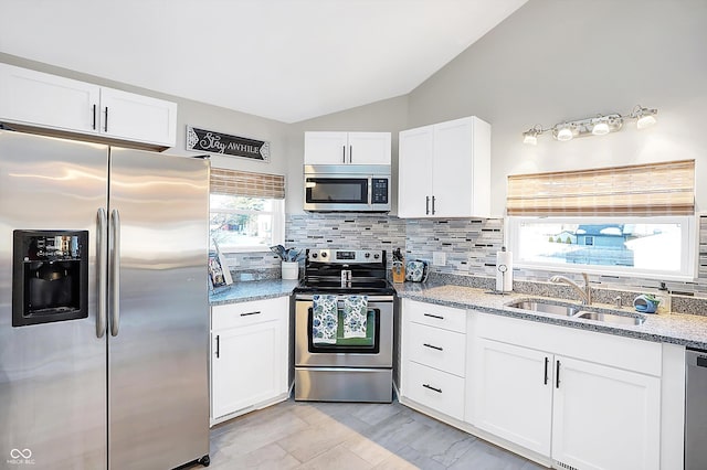 kitchen with lofted ceiling, decorative backsplash, sink, stainless steel appliances, and white cabinets