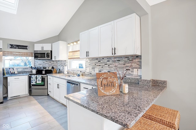 kitchen with white cabinetry, kitchen peninsula, stainless steel appliances, vaulted ceiling, and a breakfast bar