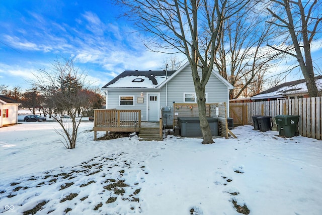 snow covered rear of property featuring a hot tub and a deck