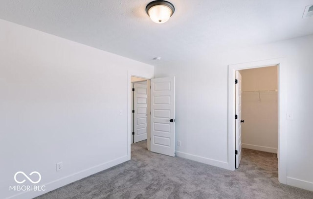 unfurnished bedroom featuring a walk in closet, a closet, and light colored carpet