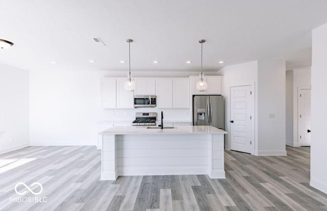 kitchen with white cabinets, appliances with stainless steel finishes, sink, hanging light fixtures, and a center island with sink