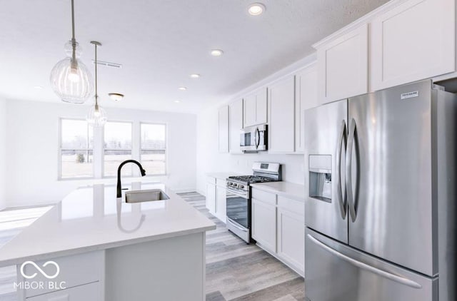 kitchen with an island with sink, appliances with stainless steel finishes, decorative light fixtures, white cabinets, and sink