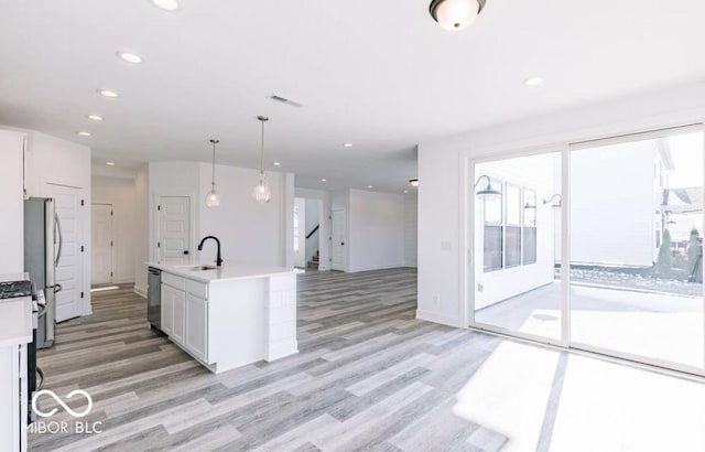 kitchen featuring white cabinets, stainless steel appliances, sink, hanging light fixtures, and a center island with sink