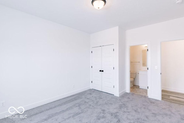 unfurnished bedroom with a closet, ensuite bathroom, and light colored carpet