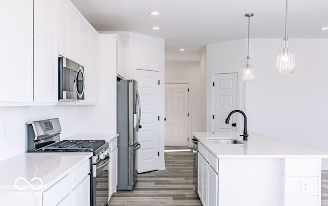 kitchen featuring appliances with stainless steel finishes, white cabinetry, sink, hanging light fixtures, and a kitchen island with sink