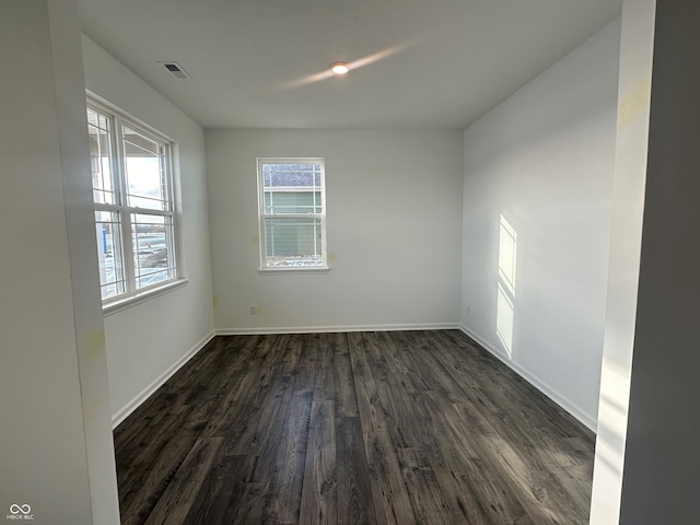 unfurnished room with baseboards, visible vents, and dark wood-type flooring