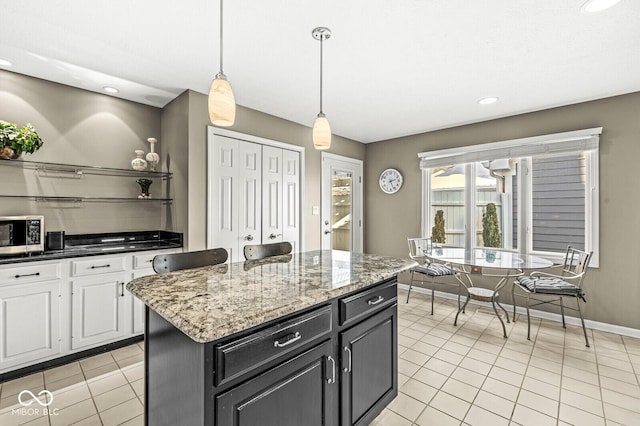 kitchen with light tile patterned flooring, white cabinetry, light stone counters, hanging light fixtures, and a kitchen island