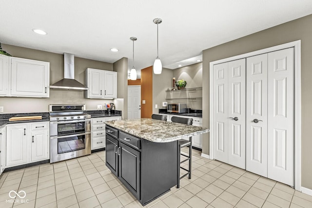 kitchen featuring wall chimney exhaust hood, a center island, appliances with stainless steel finishes, pendant lighting, and white cabinets