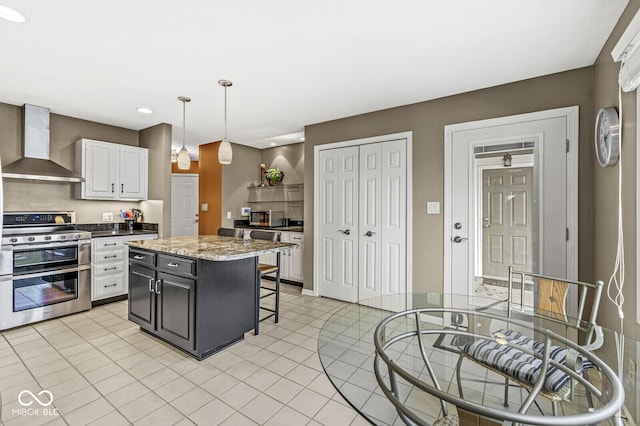 kitchen with a kitchen island, decorative light fixtures, white cabinetry, range with two ovens, and wall chimney range hood