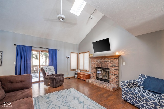 living room with a skylight, hardwood / wood-style floors, a brick fireplace, ceiling fan, and high vaulted ceiling