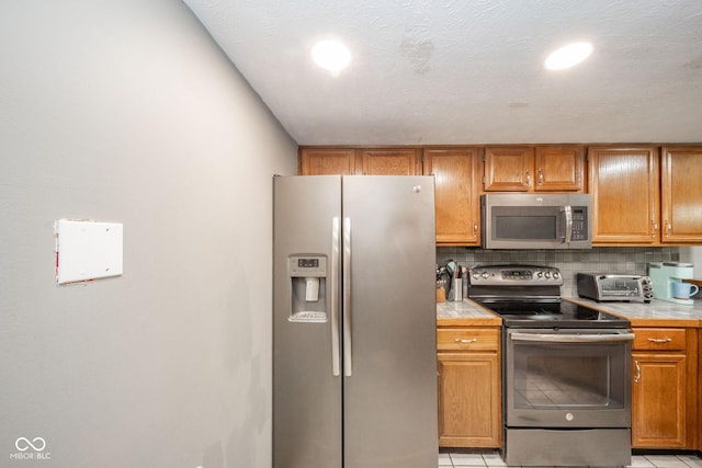 kitchen featuring a textured ceiling, light tile patterned floors, stainless steel appliances, and tasteful backsplash