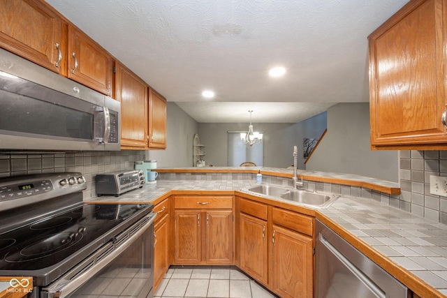 kitchen with sink, an inviting chandelier, appliances with stainless steel finishes, tile counters, and light tile patterned floors