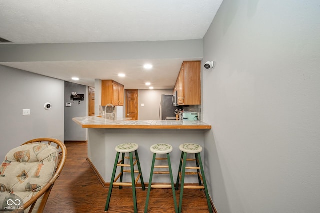 kitchen with dark hardwood / wood-style flooring, decorative backsplash, kitchen peninsula, tile countertops, and a breakfast bar area