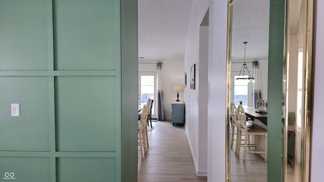 hallway with a chandelier, light hardwood / wood-style floors, and a textured ceiling