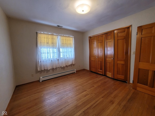 unfurnished bedroom featuring baseboard heating, a closet, and wood-type flooring