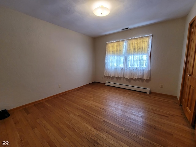 unfurnished bedroom featuring hardwood / wood-style flooring and a baseboard heating unit