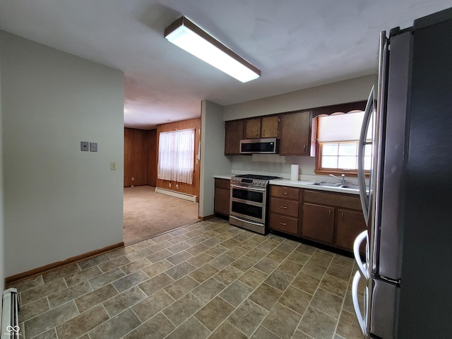 kitchen with wood walls, sink, dark brown cabinetry, stainless steel appliances, and a baseboard radiator