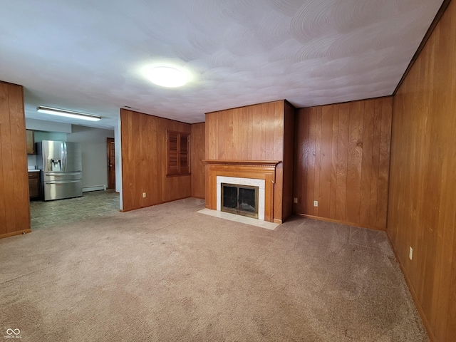 unfurnished living room featuring baseboard heating, wood walls, and carpet floors