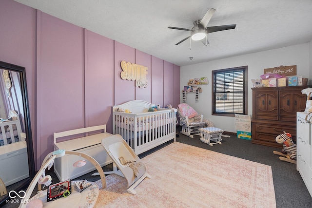 carpeted bedroom with ceiling fan and a nursery area