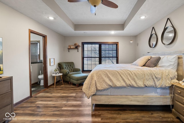 bedroom featuring ceiling fan, ensuite bathroom, a raised ceiling, and dark hardwood / wood-style flooring