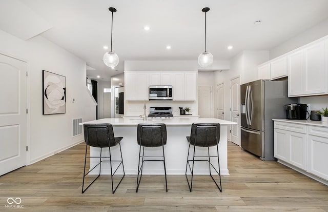 kitchen featuring a center island with sink, stainless steel appliances, white cabinetry, and decorative light fixtures