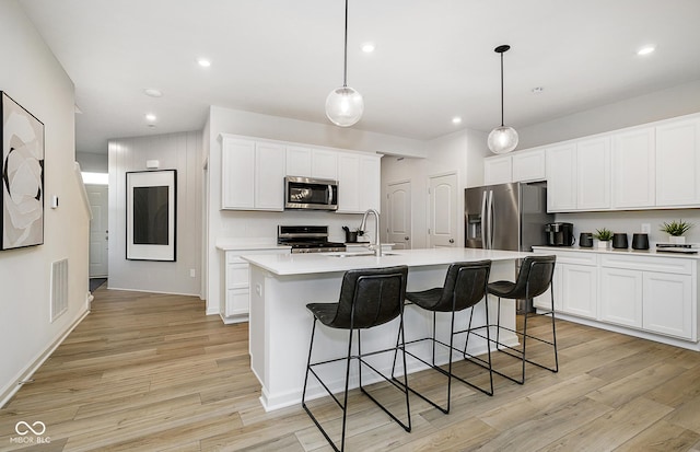 kitchen with a center island with sink, appliances with stainless steel finishes, pendant lighting, light hardwood / wood-style flooring, and sink