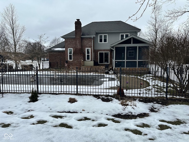 snow covered back of property with a sunroom