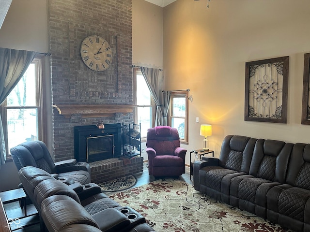 living room with a brick fireplace, a wealth of natural light, a towering ceiling, and hardwood / wood-style floors