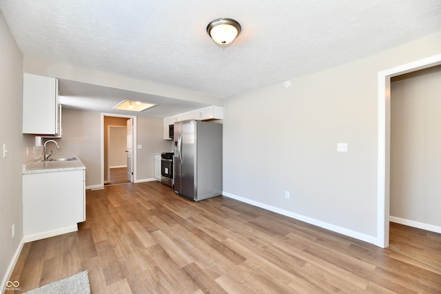 kitchen with a textured ceiling, white cabinetry, stainless steel appliances, sink, and light wood-type flooring