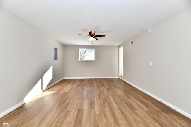 spare room with light wood-type flooring, ceiling fan, electric panel, and a textured ceiling