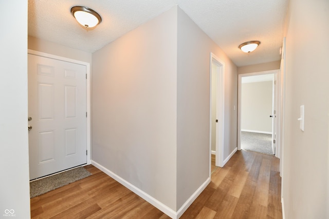 corridor with a textured ceiling and light hardwood / wood-style floors